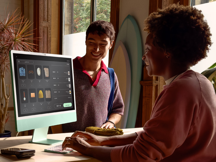 شخصان في غرفة مضاءة جيداً، أحدهما يتحقق من طلب على iMac أخضر بشريحة&nbsp;M4‏.
