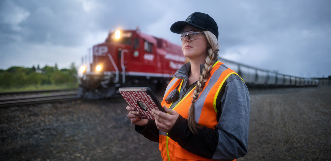 A railroad worker holds an iPad and looks out at the tracks as a train passes by
