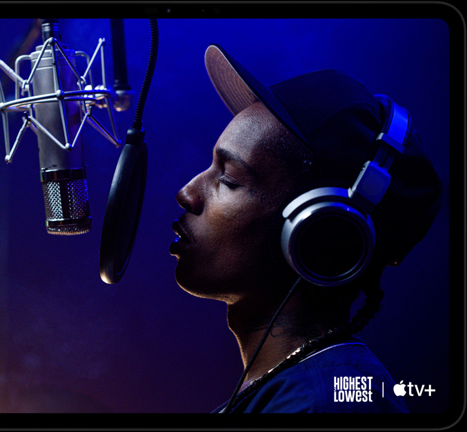 iPad Pro, хоризонтална ориентация, предна страна, цвят астро черно, заоблени ъгли, черна рамка на дисплея, дисплей, показващ AppleTV+, възпроизвеждащ сцена от оригиналния филм на Apple TV+ „Highest 2 Lowest“ с ASAP Rocky като Yung Felon, който рапира в микрофон