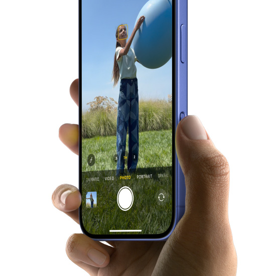 Hand holding an iPhone 16 in Ultramarine, with the thumb sliding along the Camera Control button to select the Photo feature